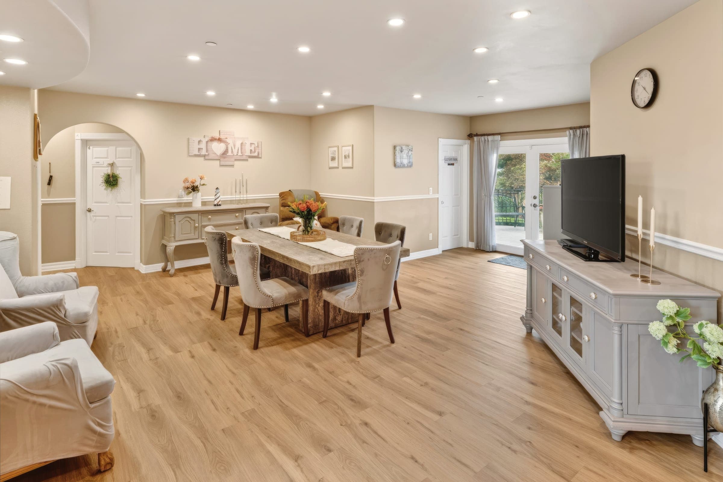 Dining area with a long wooden table, fresh flowers, and a “HOME” sign on the wall