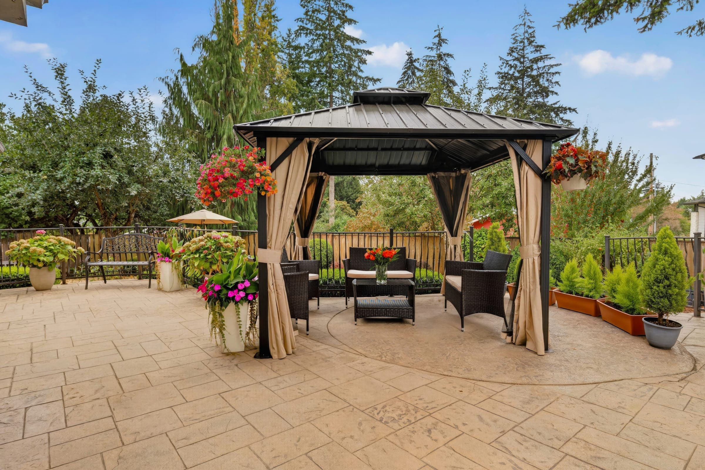 Gazebo with outdoor seating, surrounded by flowers and evergreen trees